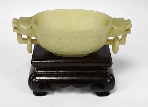 A Chinese archaistic pale green bowenite jade twin handled cup on stand, cup 11.5cm wide. Condition - cup good, stand good